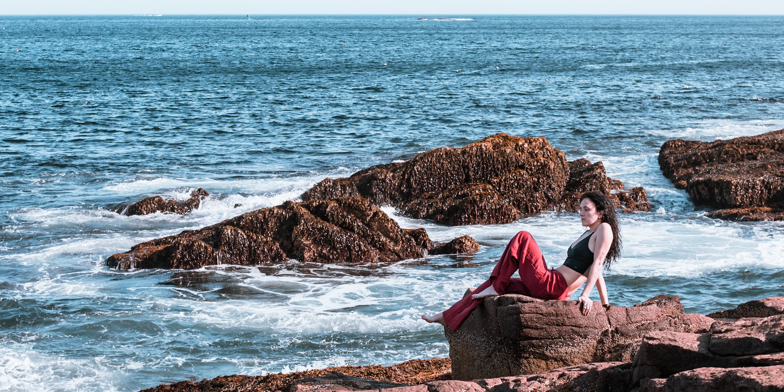 Woman in red trousers reclining on rocks above breaking surf